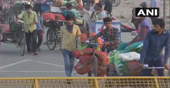 दिल्ली में कोरोना वायरस महामारी के बीच गाज़ीपुर फल और सब्जी मंडी से खरीदारी कर सामान लाते हुए ग्राहक
