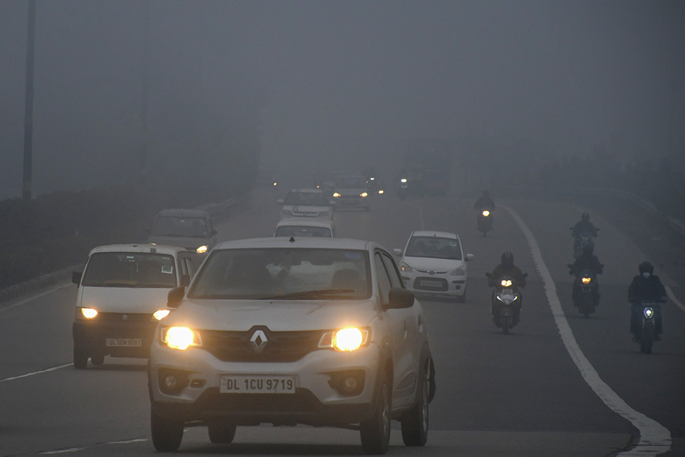 नई दिल्ली में सर्दियों की सुबह धुंध के कारण हेडलाइट्स जलाकर सड़क पर दौड़ती गाड़ियां