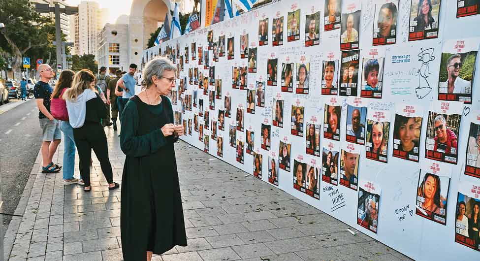 गुमशुदा लोगः तेल अवीव की दीवार पर प्रदर्शित इजरायल के गुमशुदा लोगों की तस्वीरों को देखती एक महिला